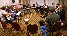 People siting in a loose circle with muscial instruments