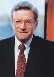 A color photograph of a man, John Silber, showing his head and upper torso, which is covered by a suit and tie